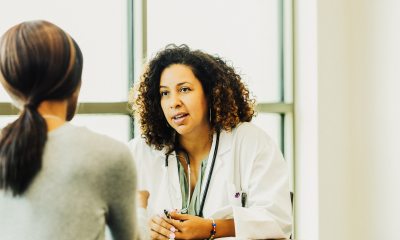 A doctor at her desk faces the camera and shares information with a female patient facing away from the camera